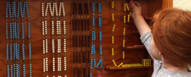 Child reaching for a string of beads in a classroom