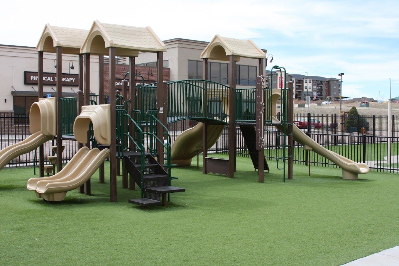 A beige and green playground with multiple slides and climbing structures