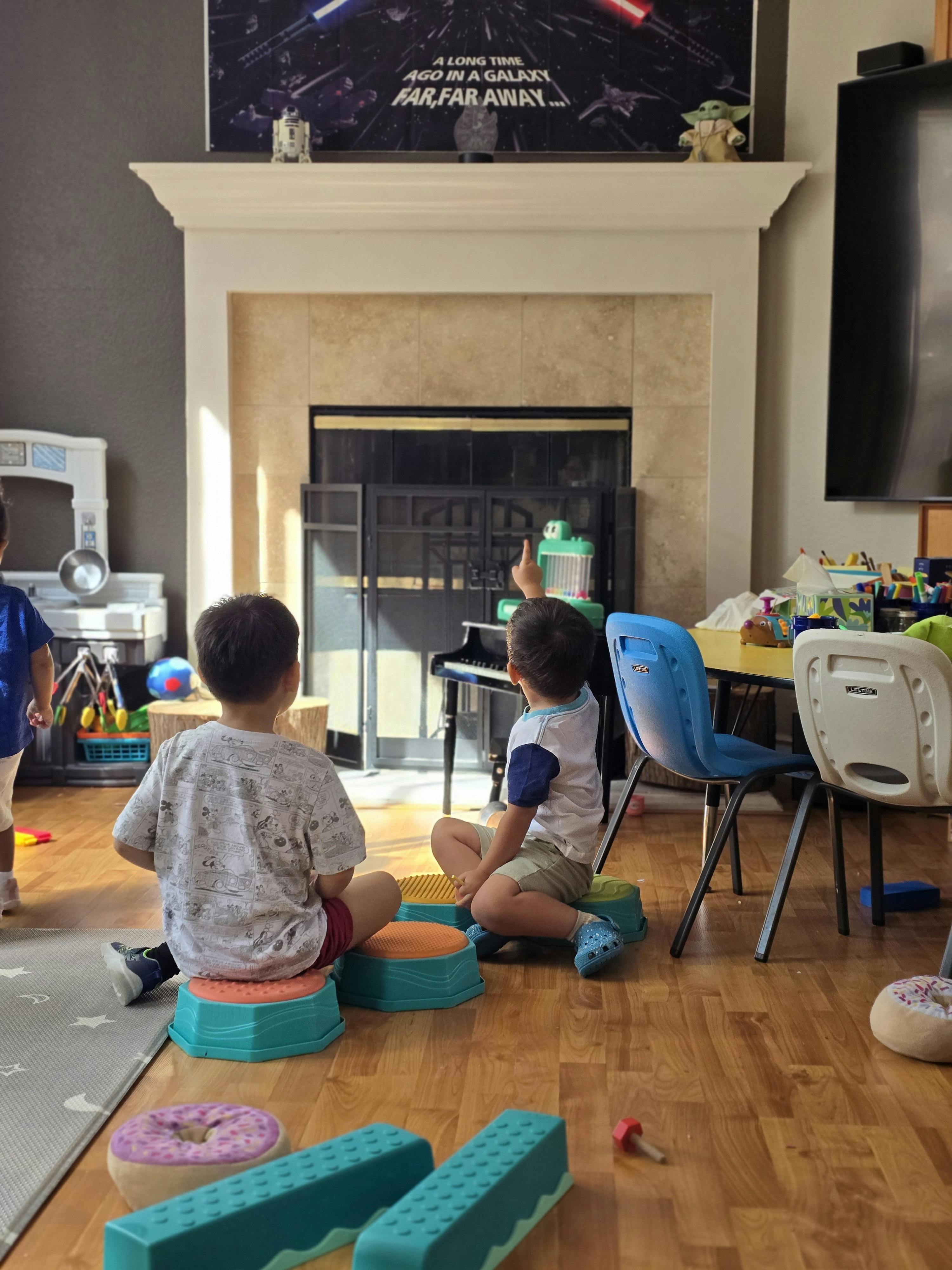 Two children sitting on small stools and pointing toward a fireplace