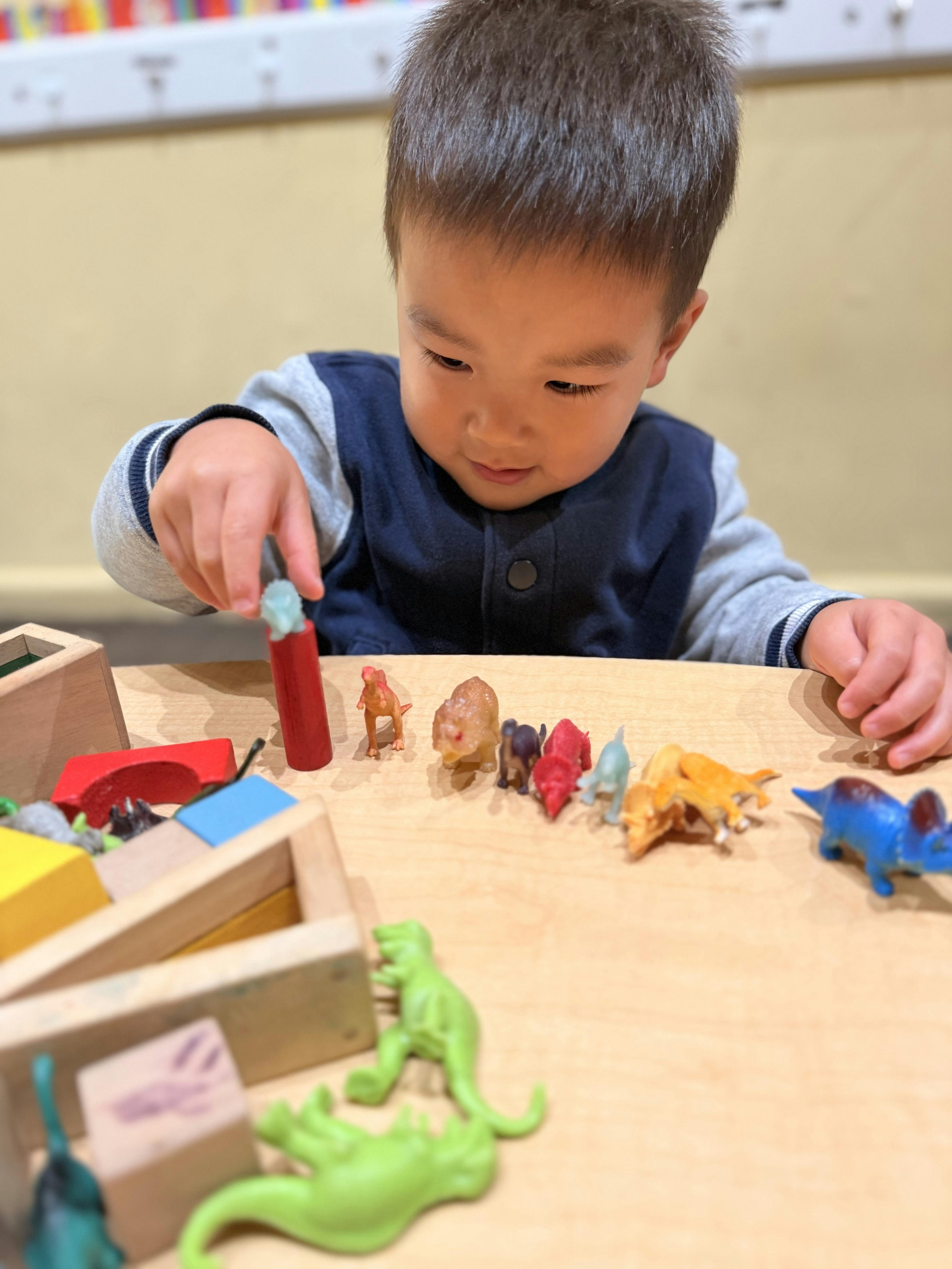Child playing with small toy dinosaurs on a wooden table