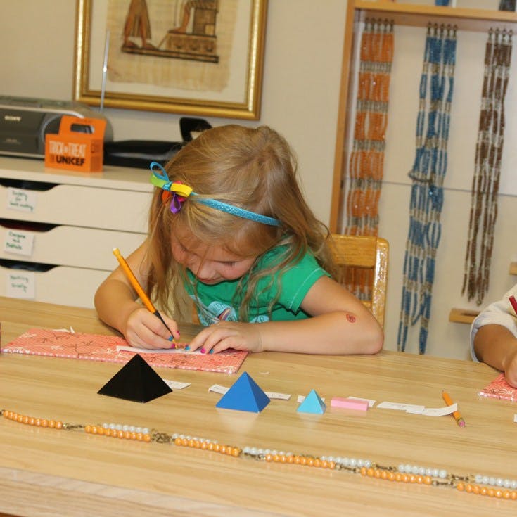 Child drawing at a table with geometric shapes