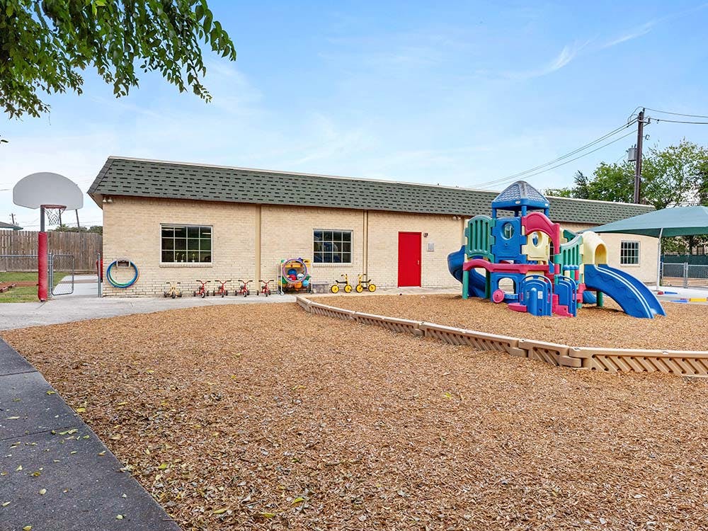 Playground with climbing structure and slides on wood chips next to a brick building