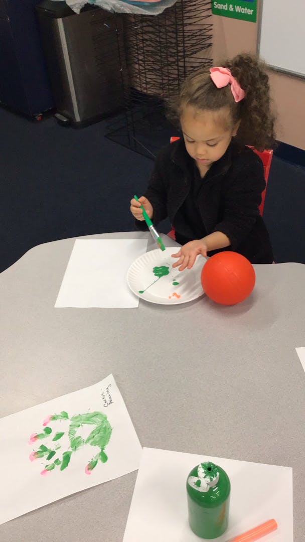 Child painting with green paint at a table