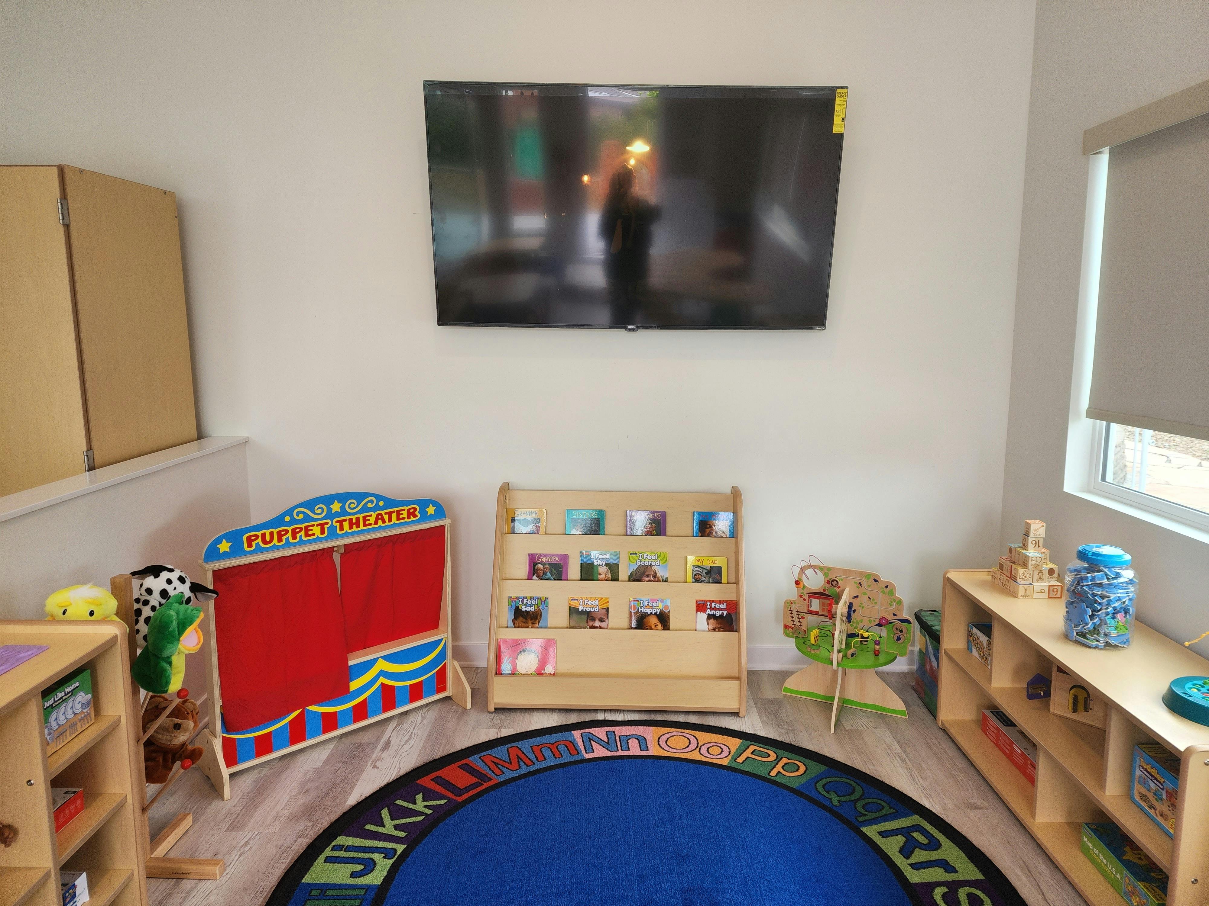 Children's play area with a puppet theater, book display, and alphabet rug