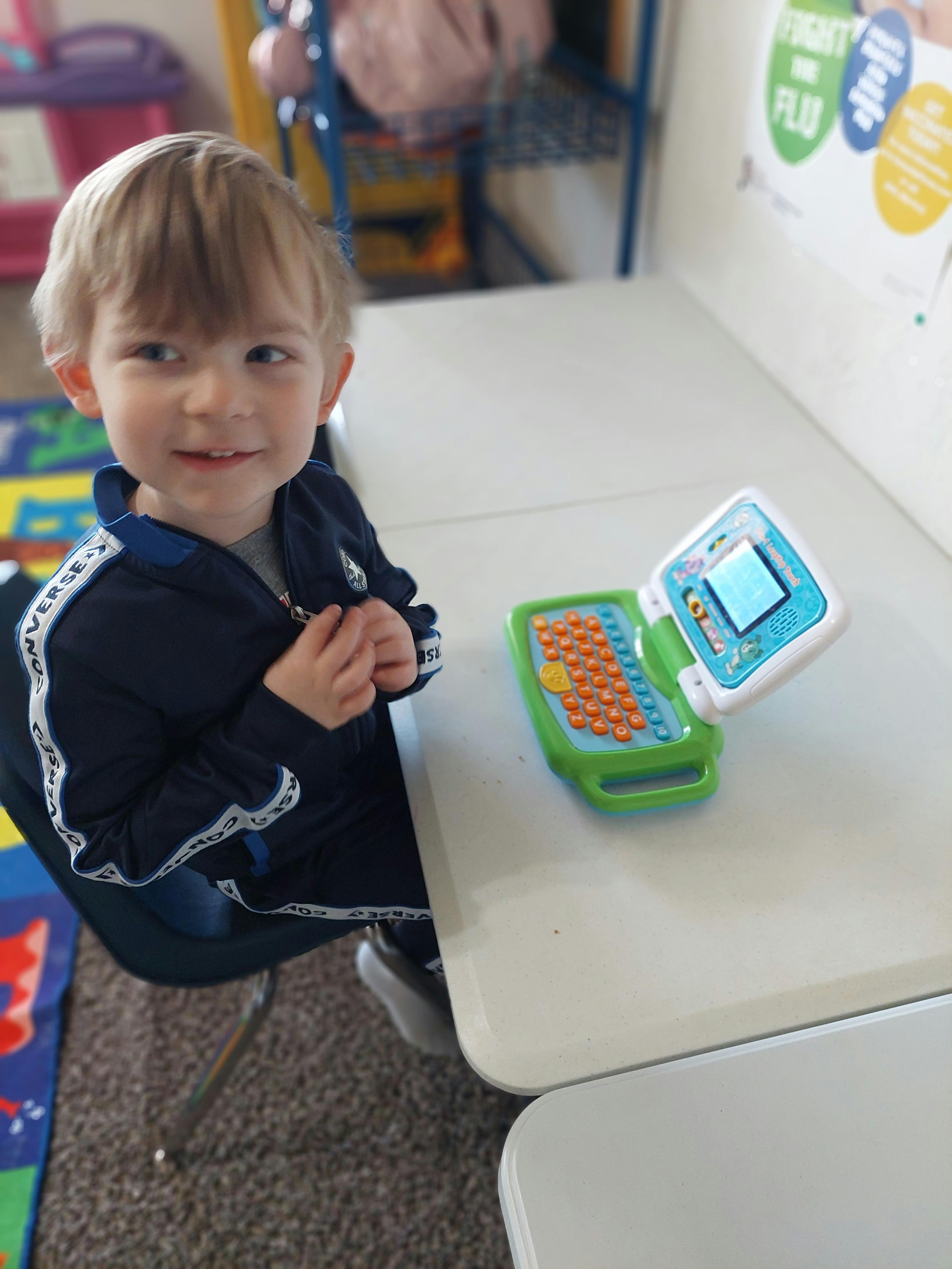 Child sitting at a desk with a toy laptop