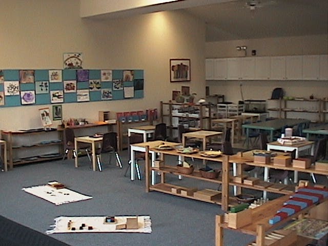 Classroom with small tables, chairs, and shelves with learning materials