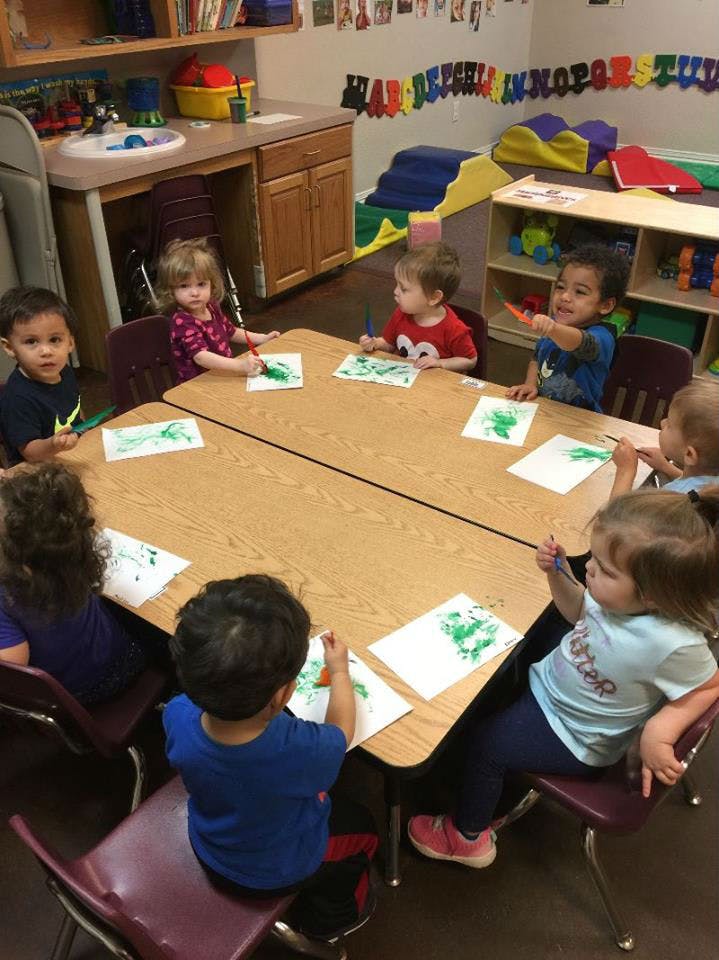 Children sitting at a table painting with green paint