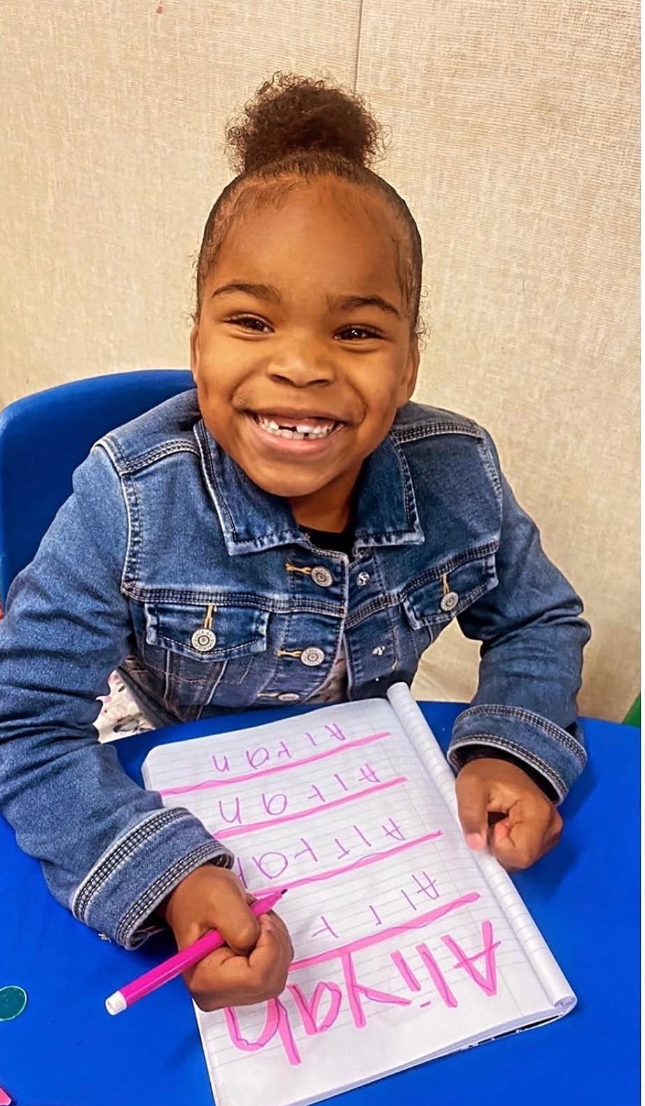 Child smiling while writing the name Aliyah in a notebook