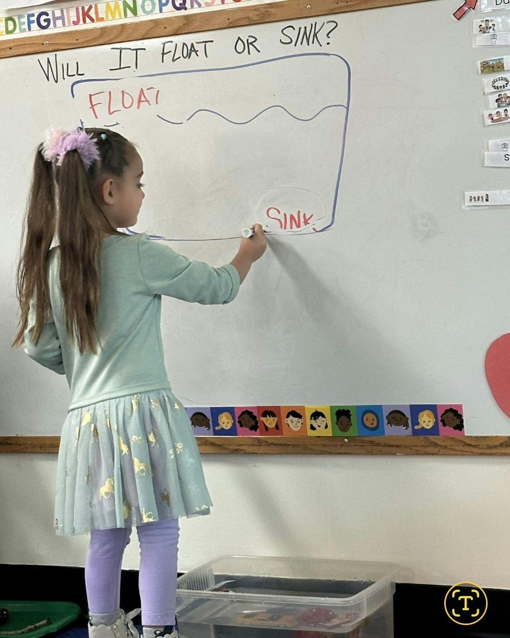 Child writing on a whiteboard with "Will it float or sink?" written on it