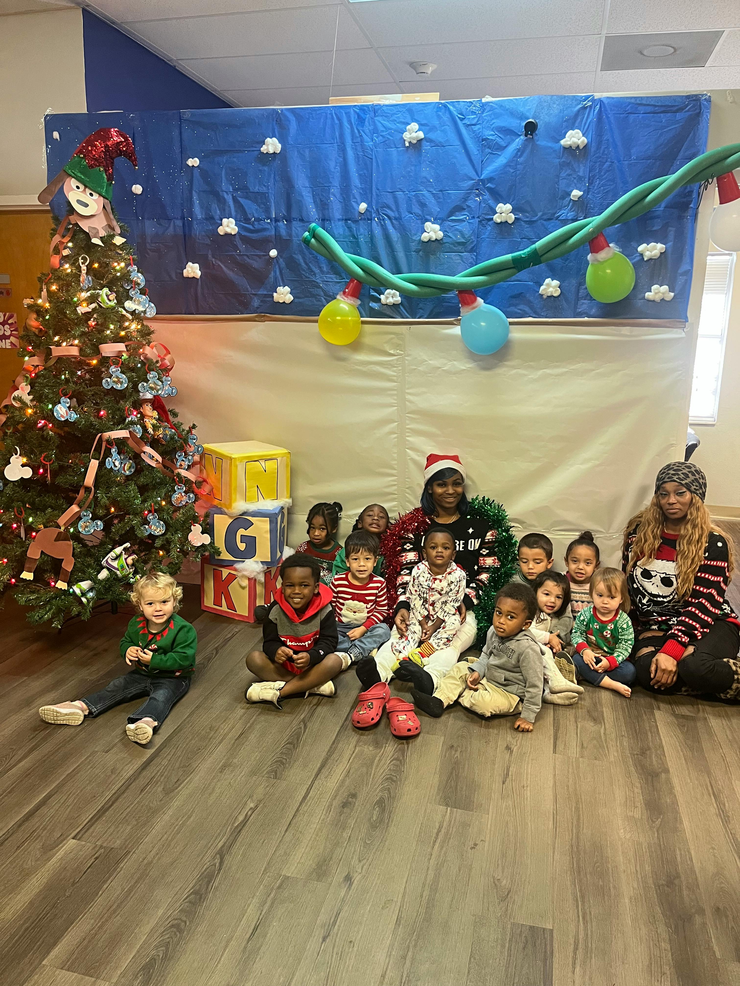 Two adults and multiple children sitting on the floor in front of a Christmas tree