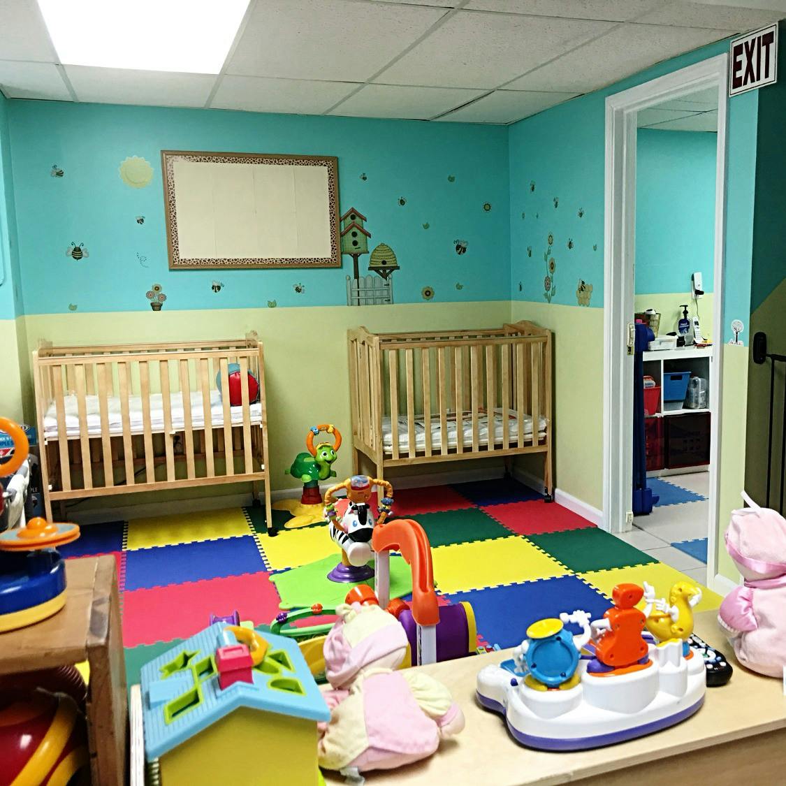 Two cribs in a room with colorful floor mats and toys