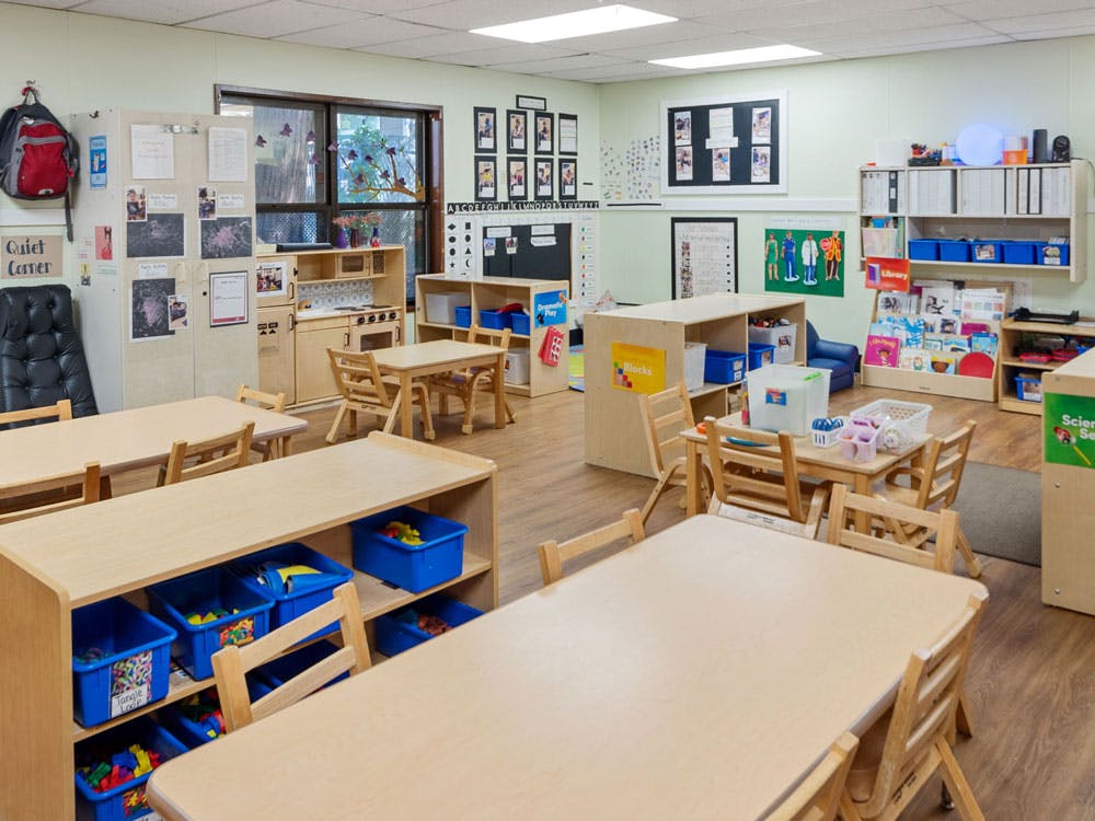 Empty children's classroom with small wooden tables and chairs, toys, and learning materials