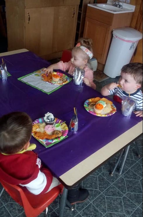 Three children sitting at a table with plates of cupcakes and cupcakes