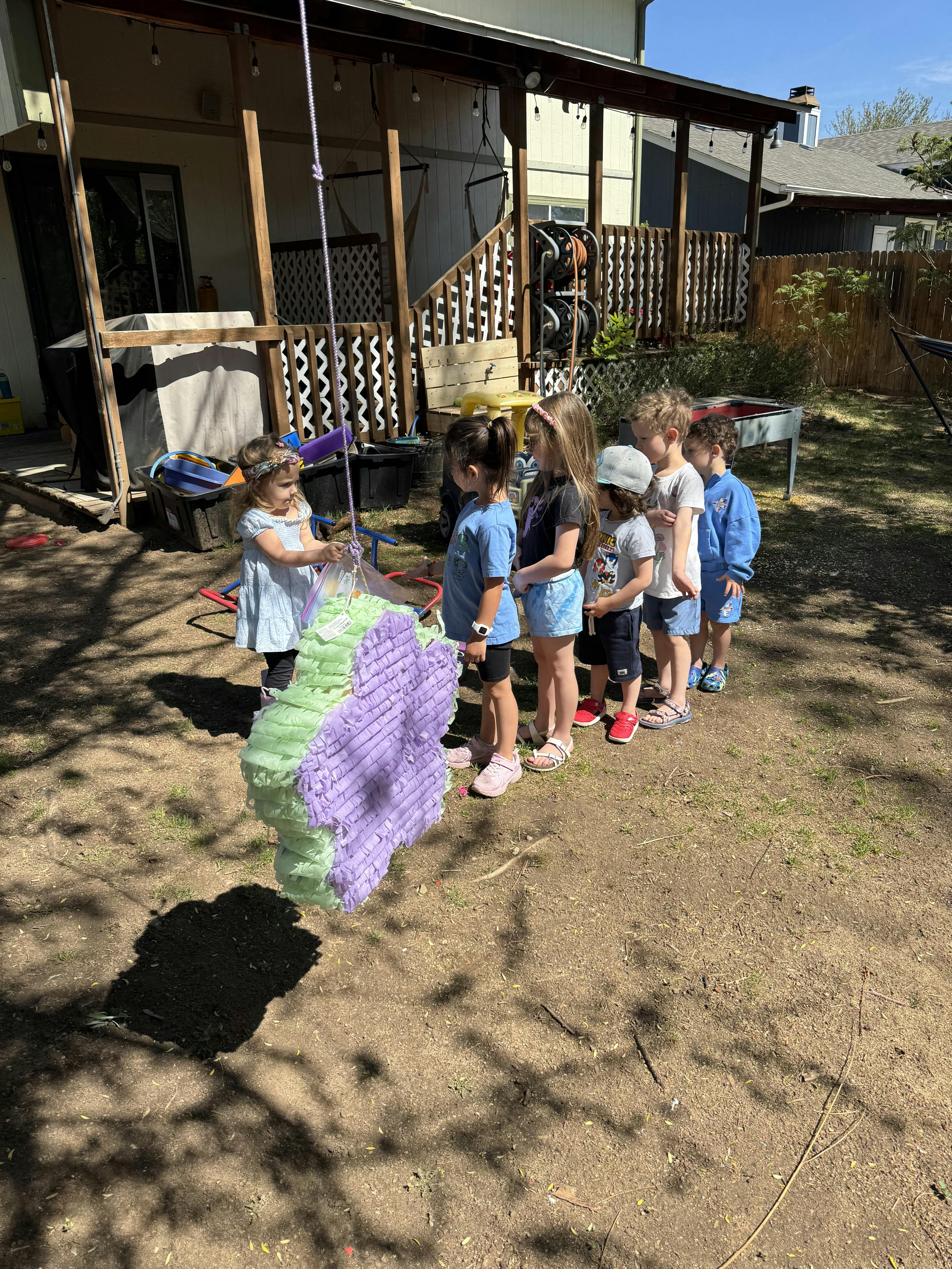 Child about to hit a butterfly piñata with other children waiting in line