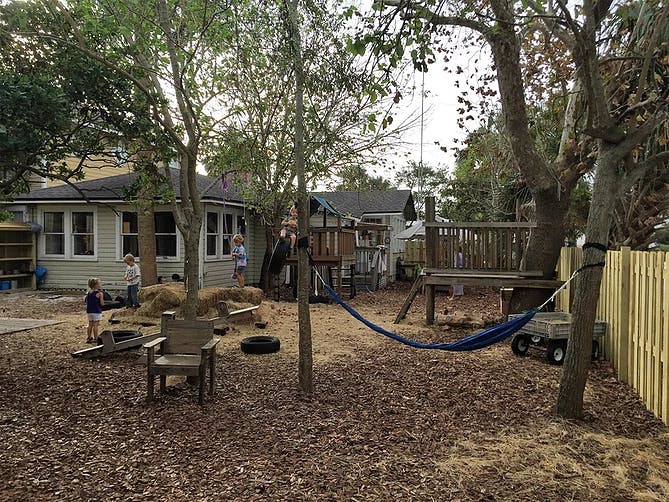 Children playing in a backyard with a play structure and hammock