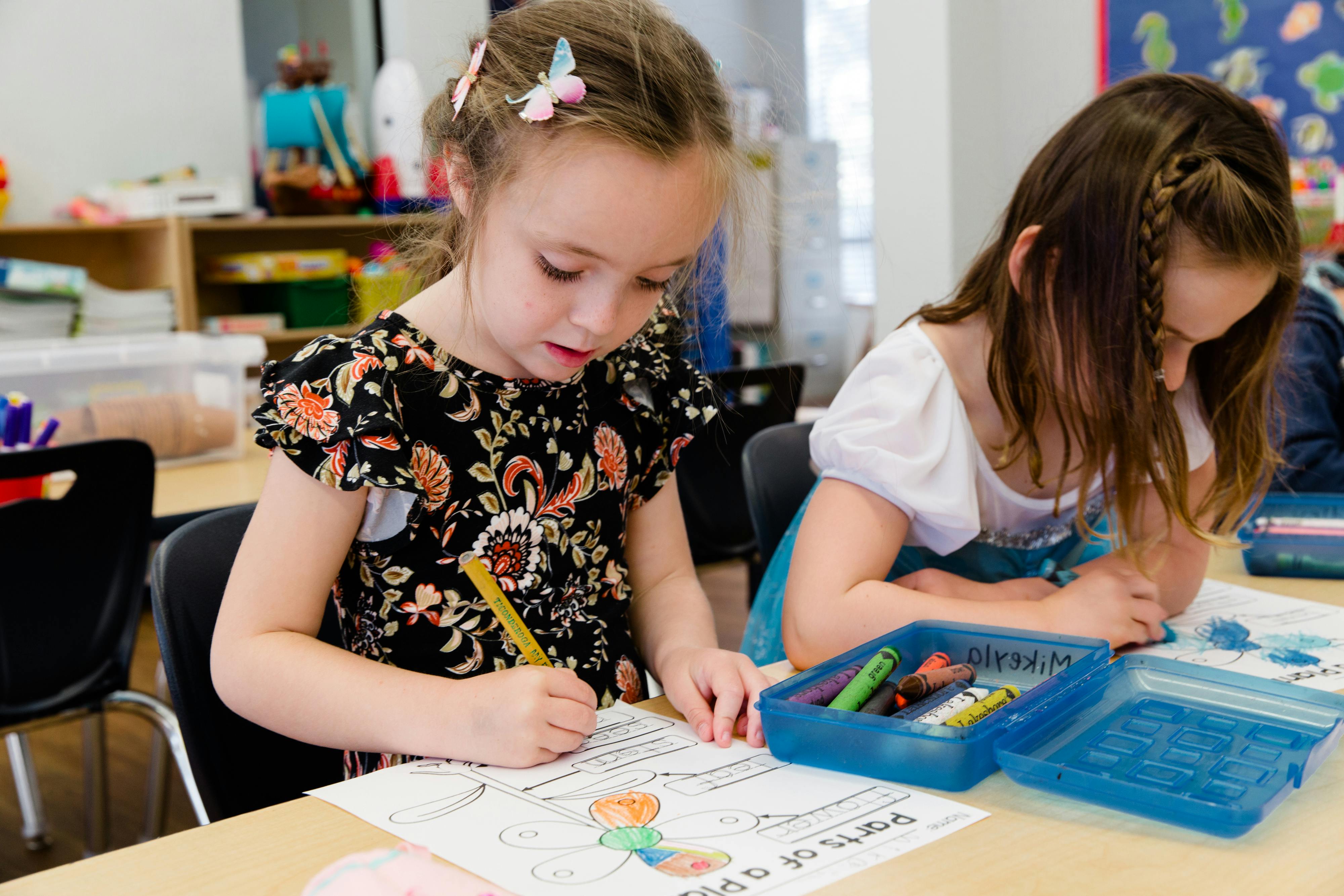 Two children drawing and coloring at a table in a classroom