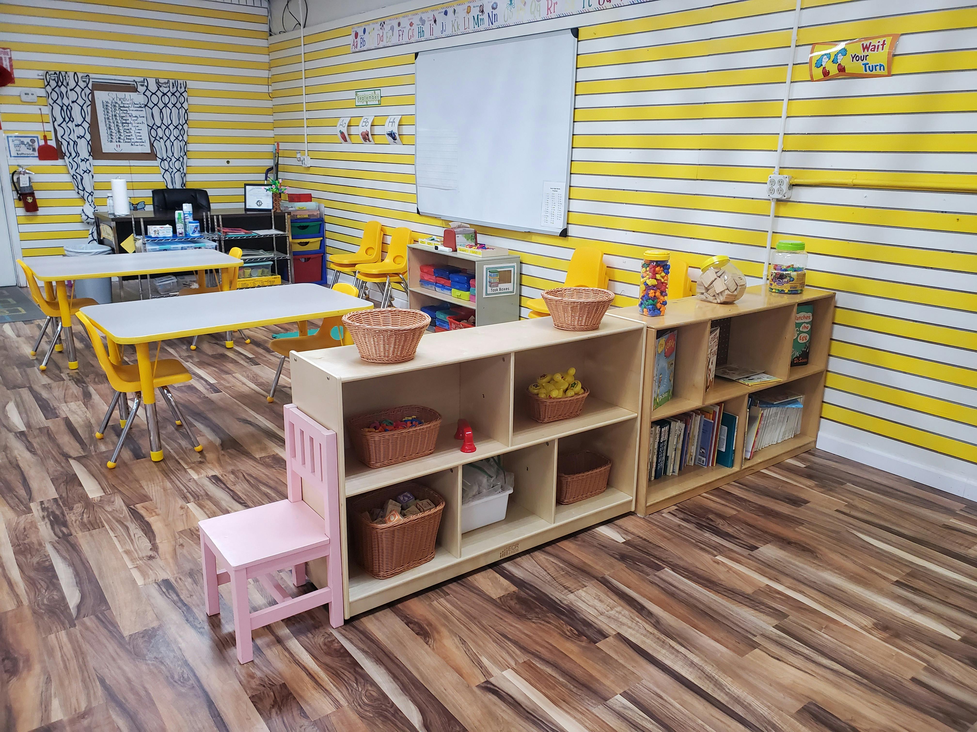 Classroom with small tables and chairs, shelves with baskets and books