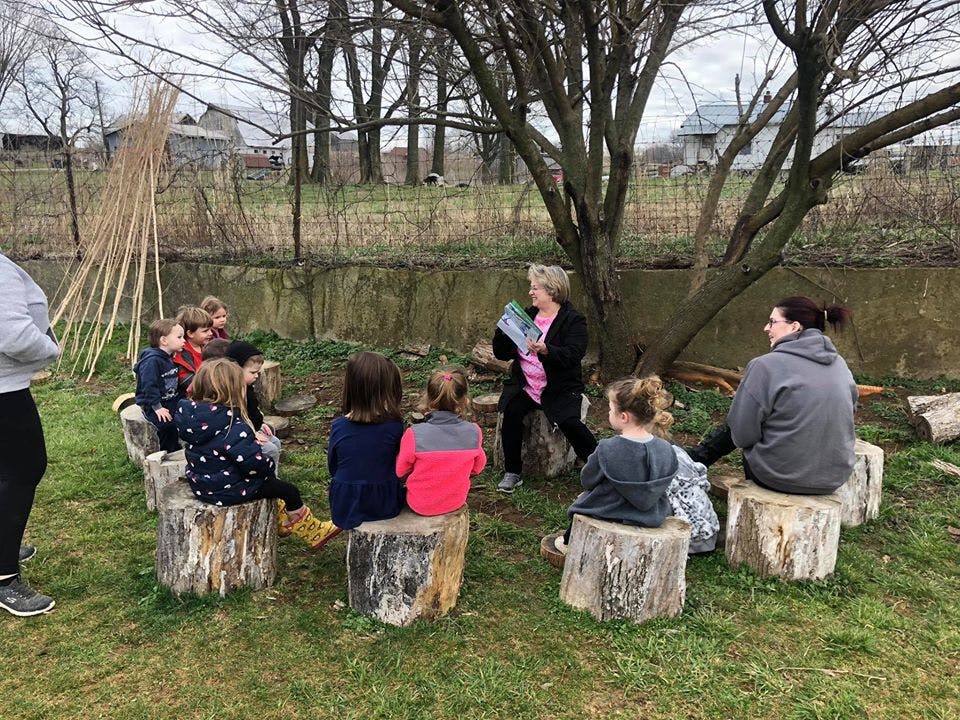 Adult reading to children sitting on tree stumps outdoors