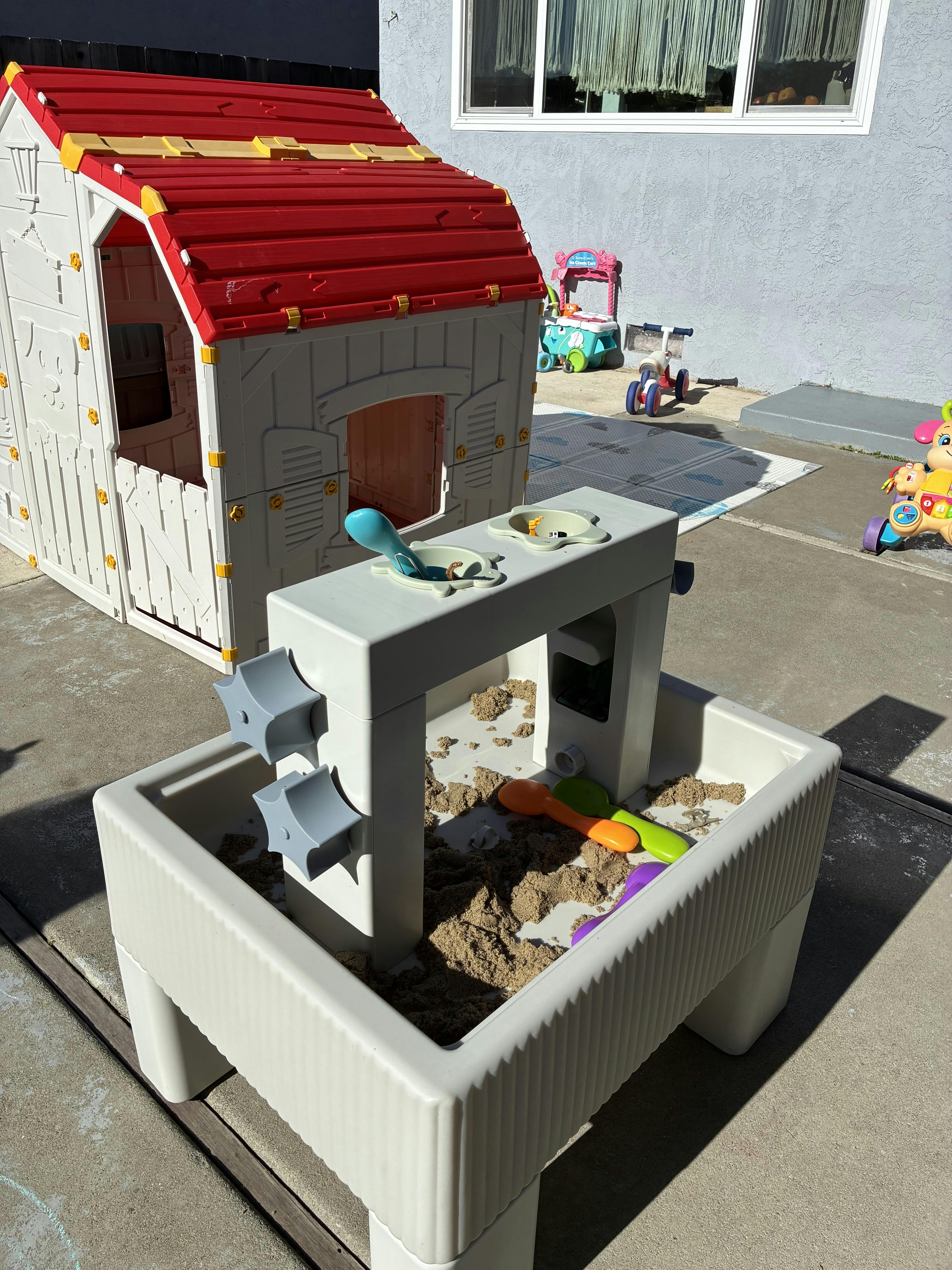 Plastic playhouse with red roof next to a sand and water play table