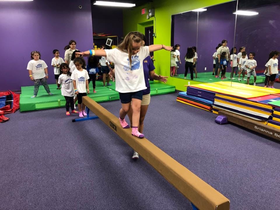 Child walking on a balance beam with arms outstretched in a gym