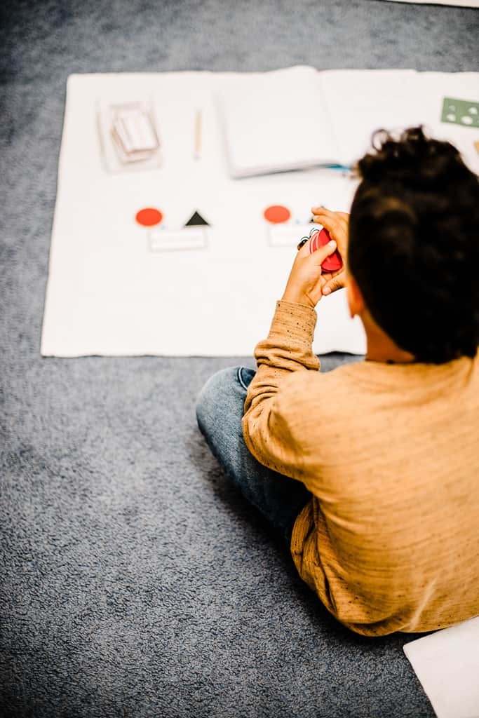 Child sitting on floor playing with red and black shapes on a white mat