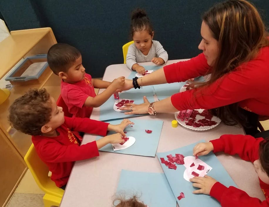 Adult and children doing crafts at a table in a classroom
