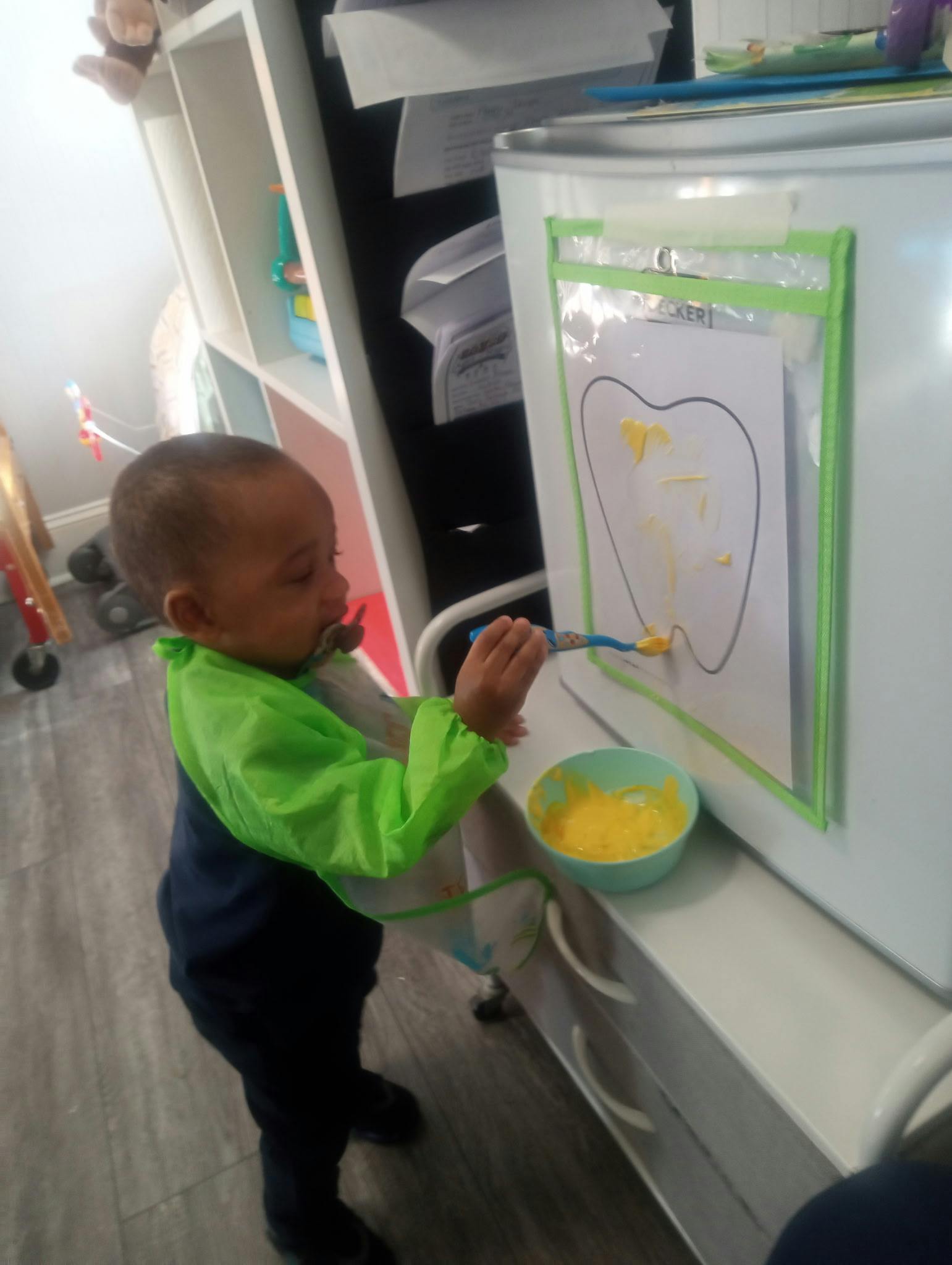 Child in an art smock painting a tooth outline on a vertical surface