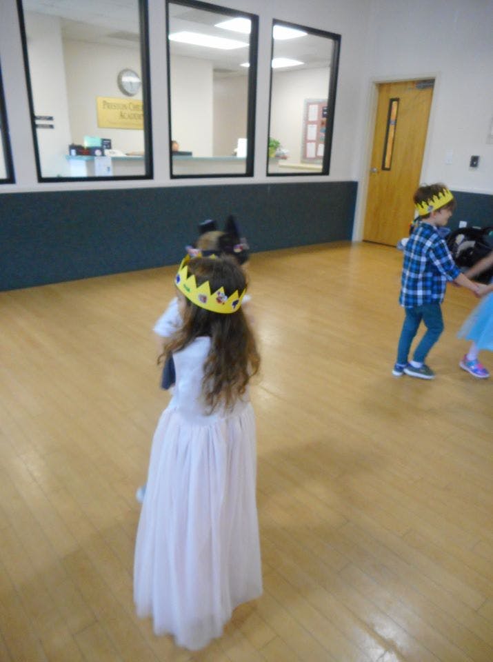 Child in a white dress and crown dancing with other children