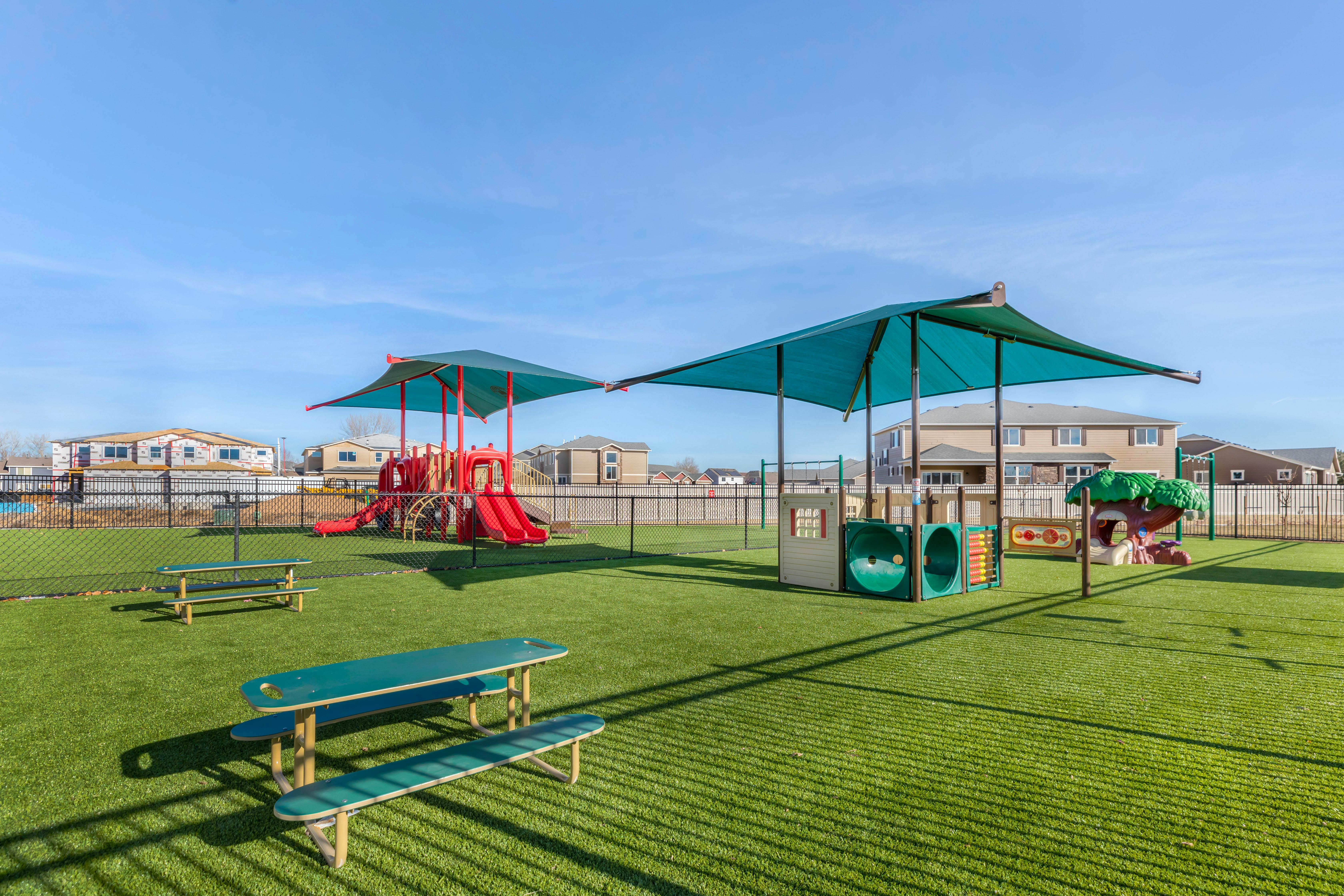 Playground with slides, climbing structures, and picnic tables on artificial turf