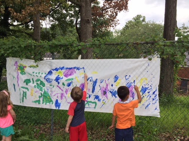 Three children painting on a large white banner outdoors