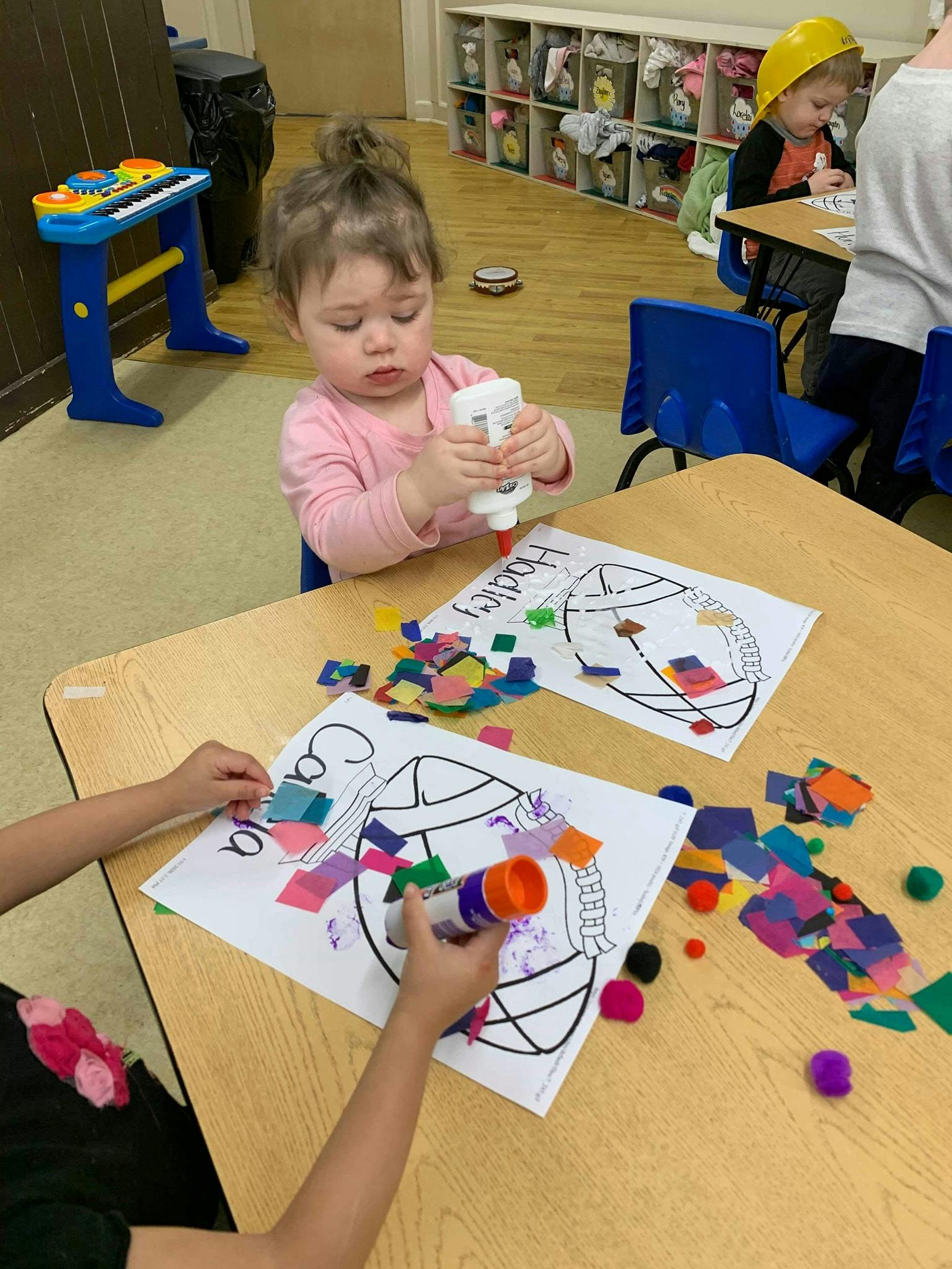 Child holding a glue bottle over a drawing with colorful paper squares