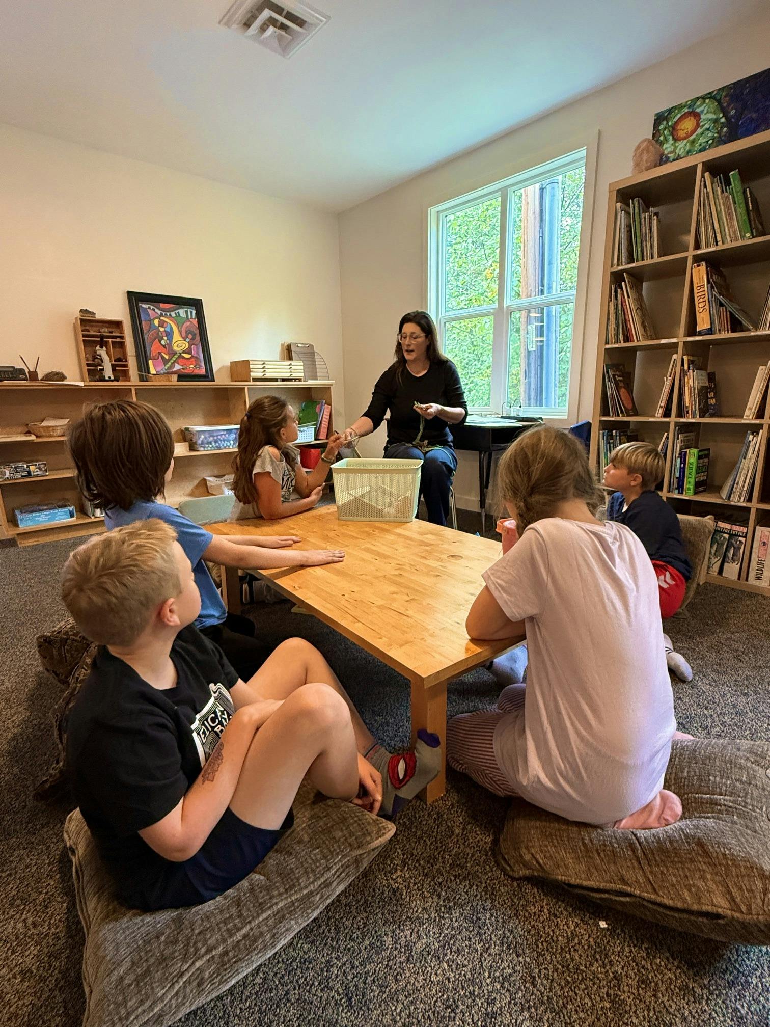 Group of children and an adult sitting on floor cushions at a table