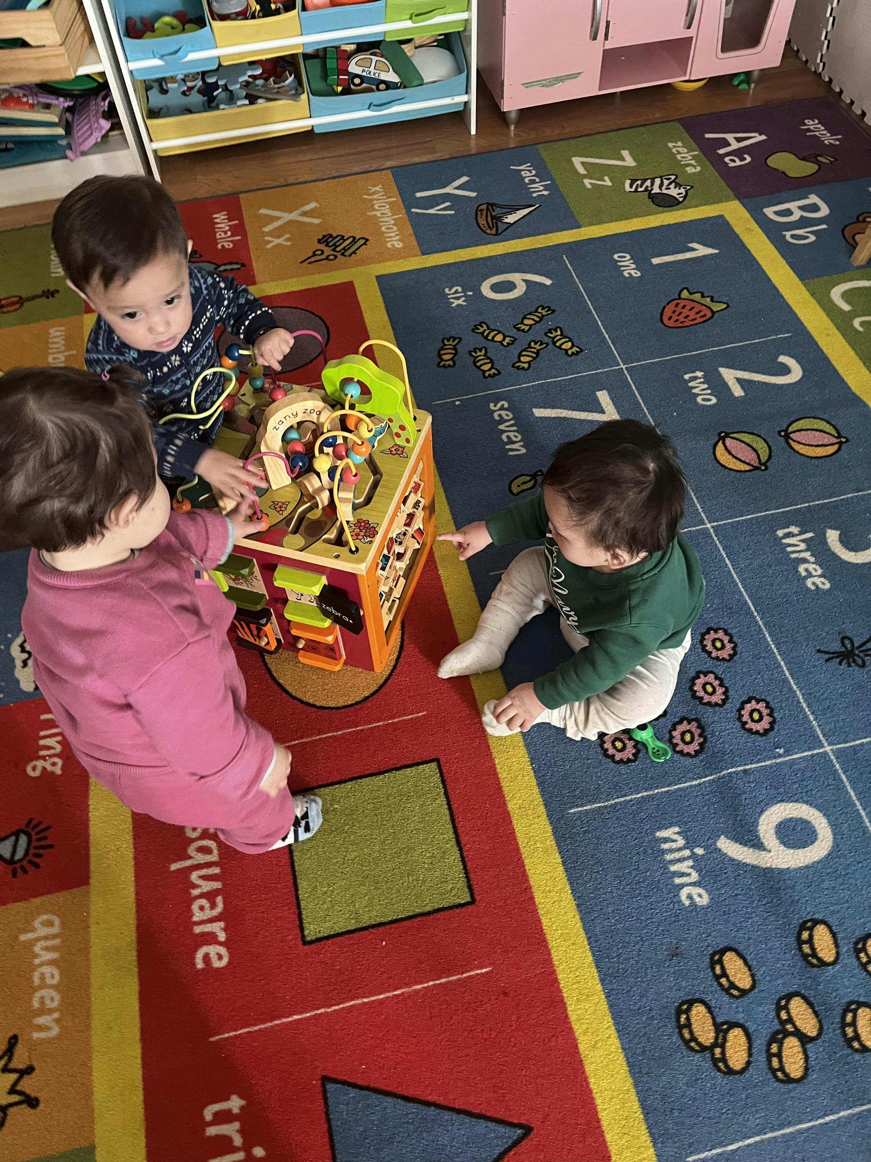 Three children playing with an activity cube on a colorful alphabet rug