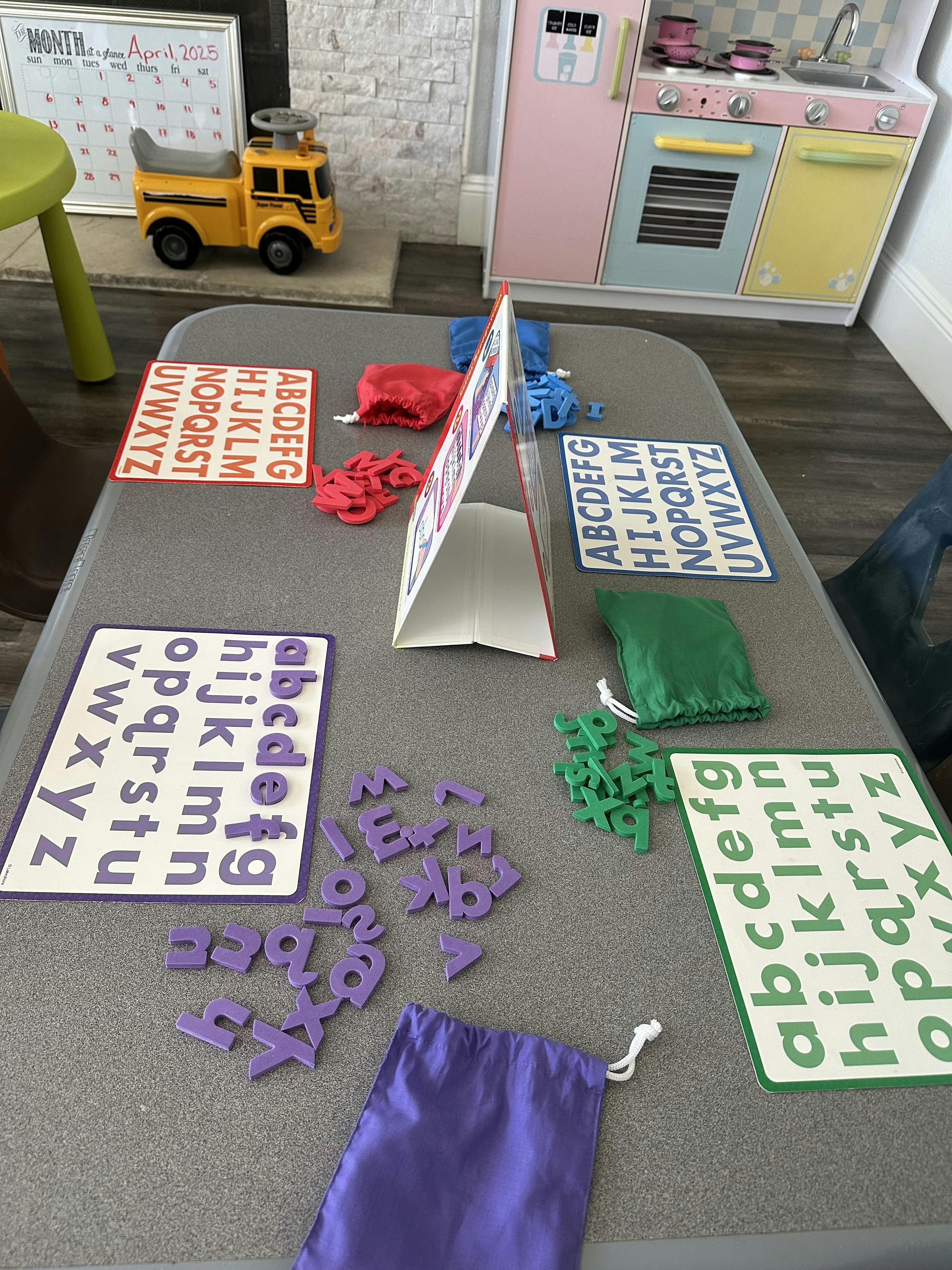 Table with alphabet learning materials and toy kitchen in background