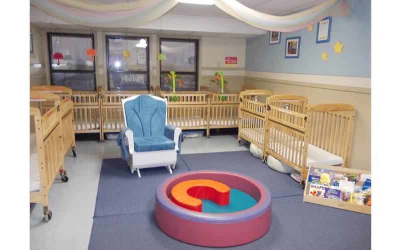 multiple wooden cribs arranged in a room with a rocking chair and a playpen