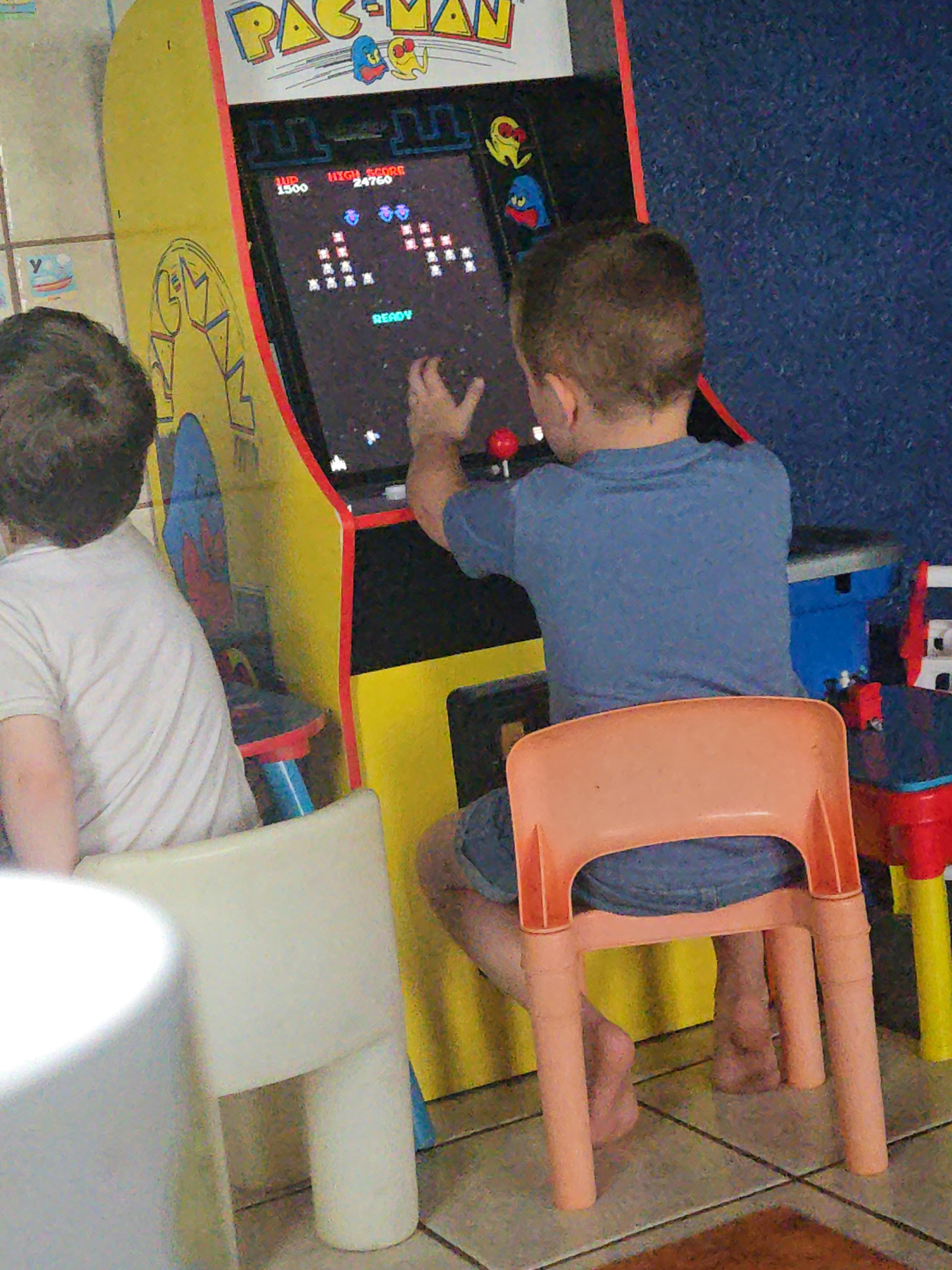 Child playing an arcade game with another child sitting nearby