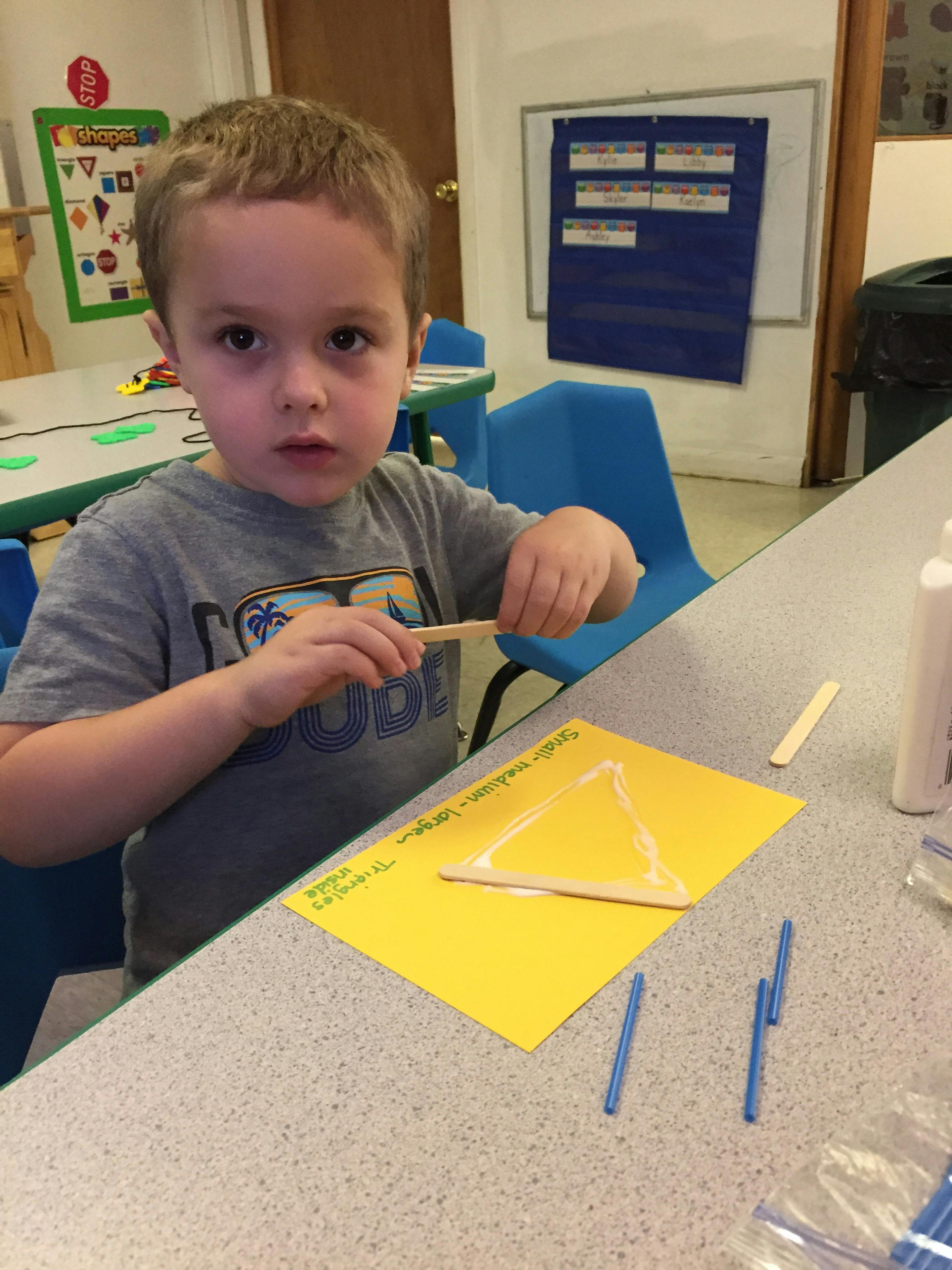 Child making a craft with popsicle sticks and glue on yellow paper