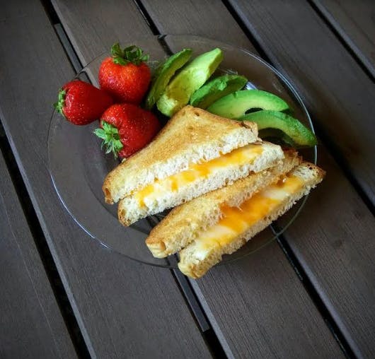 Grilled cheese sandwich halves with strawberries and avocado slices on a plate
