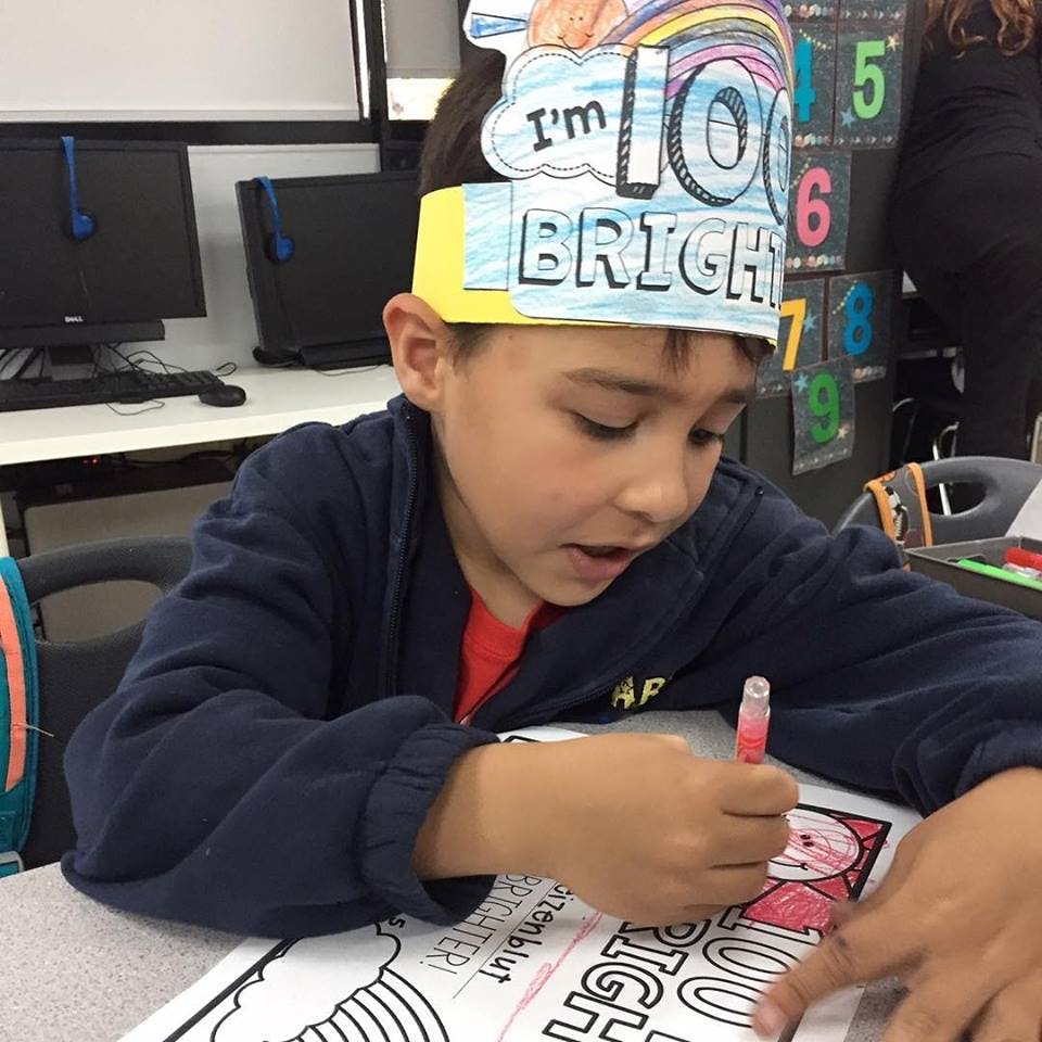 Child wearing a paper crown that says "I'm 100 BRIGHT" coloring a picture