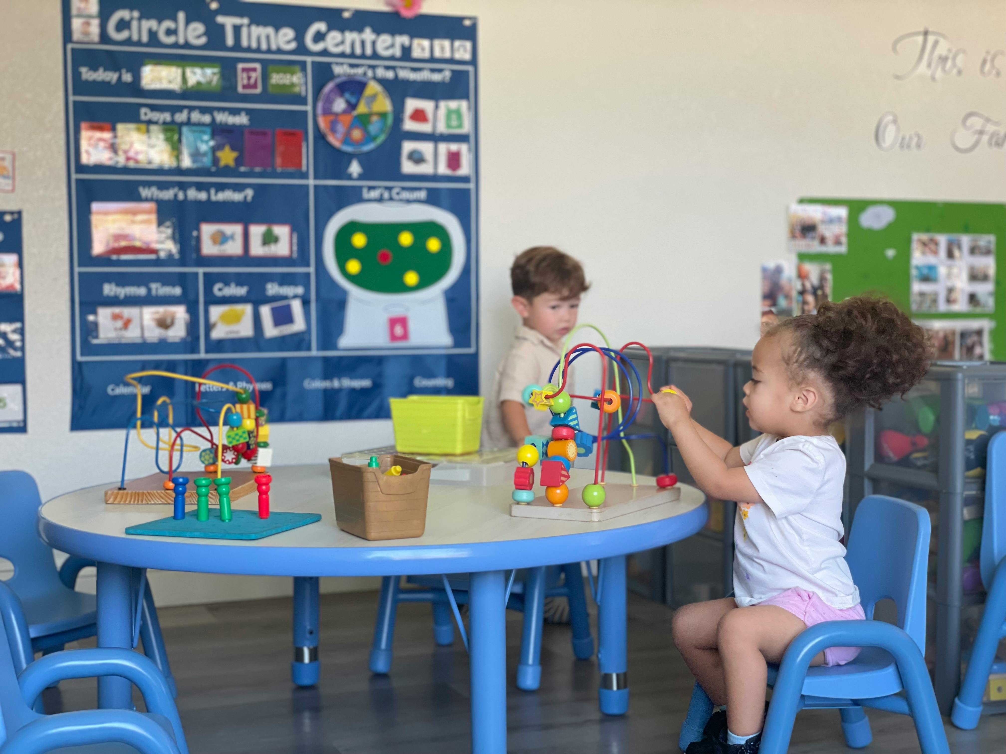 Two children playing with bead mazes at a table in a classroom
