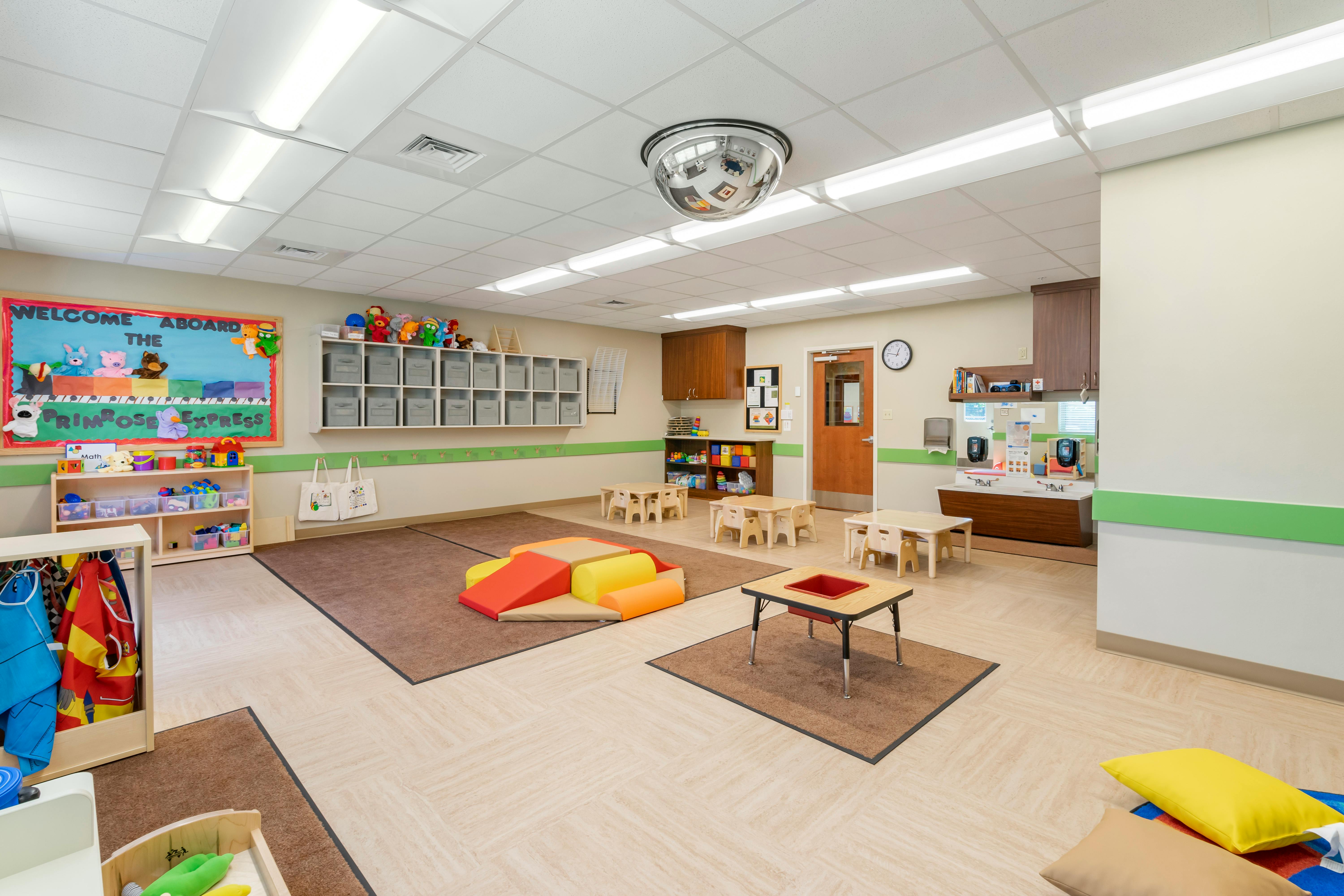 A colorful empty classroom with small tables, chairs, and play equipment