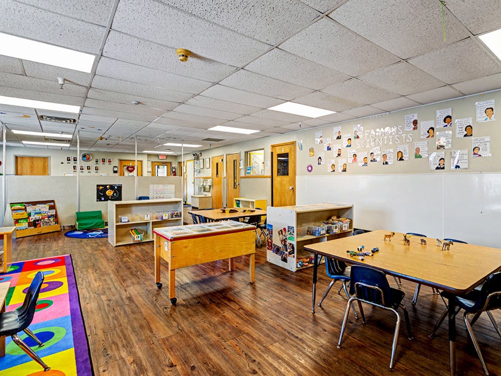 Classroom with tables, chairs, shelving units, and educational posters on walls
