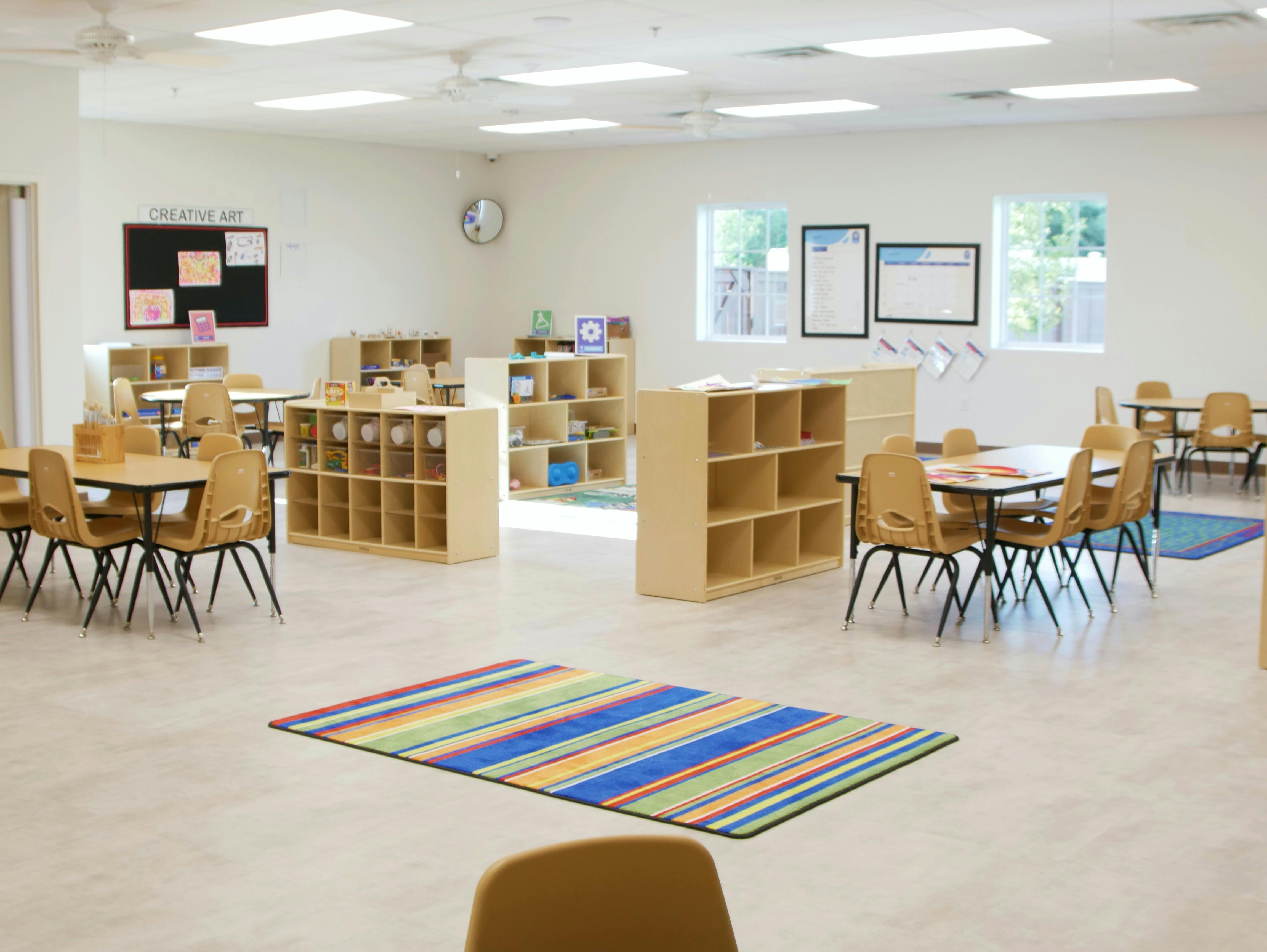 Empty classroom with small tables, chairs, and storage shelves