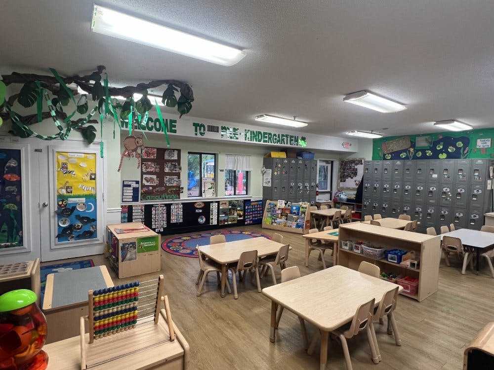 empty kindergarten classroom with small tables, chairs, and lockers