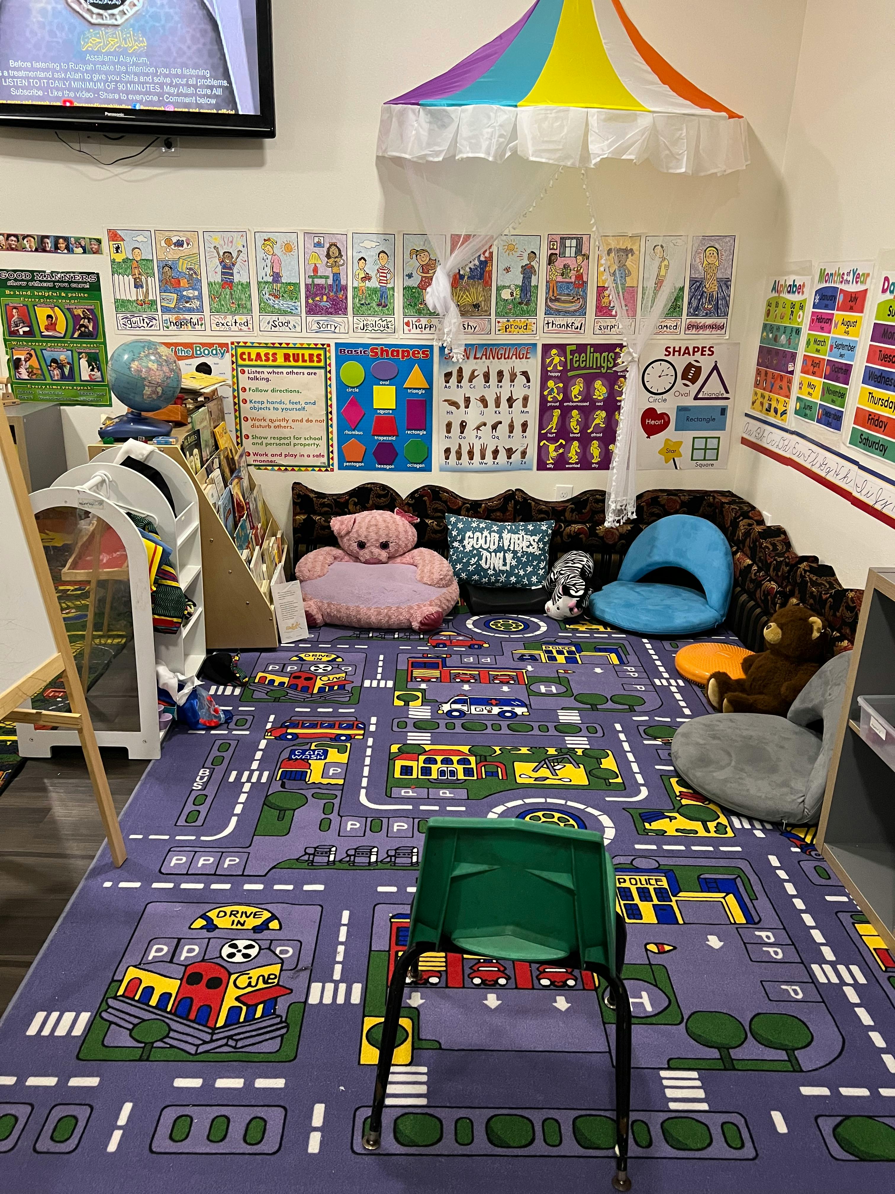 A colorful classroom with a play rug, seating, and educational posters