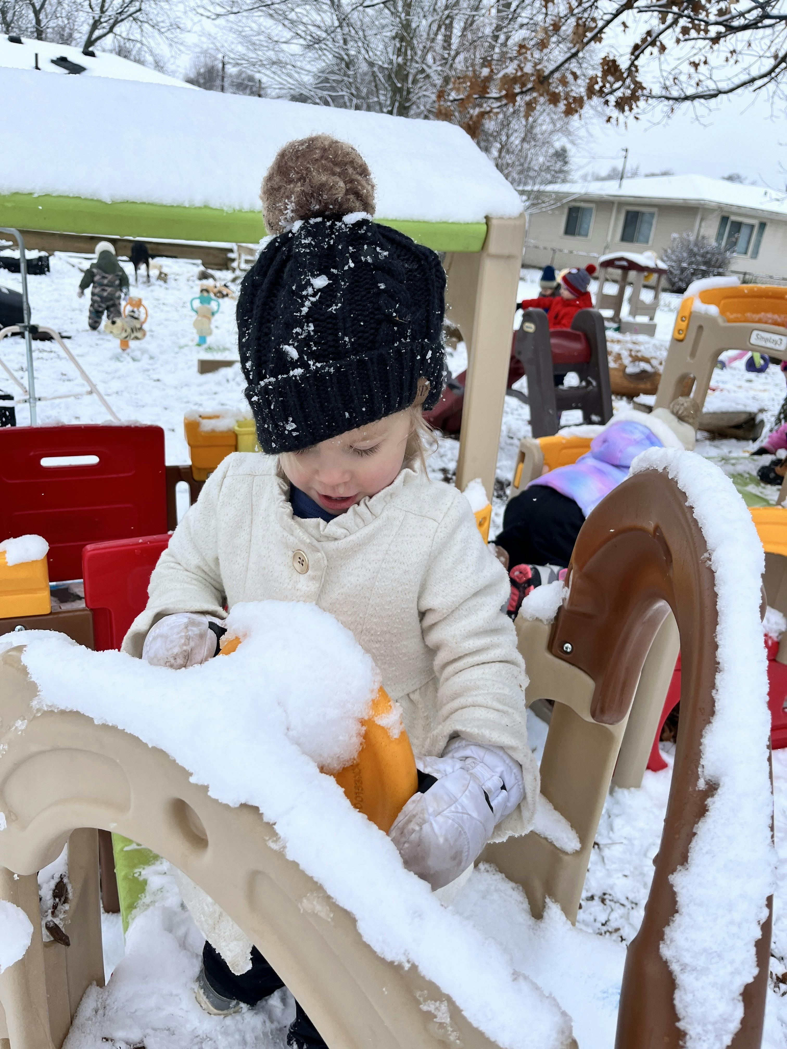 Child wearing a hat and coat playing on a snowy outdoor play set