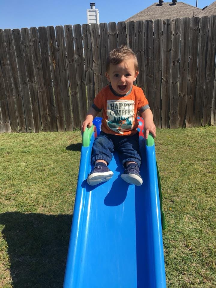 Child sitting on a blue slide in a grassy yard