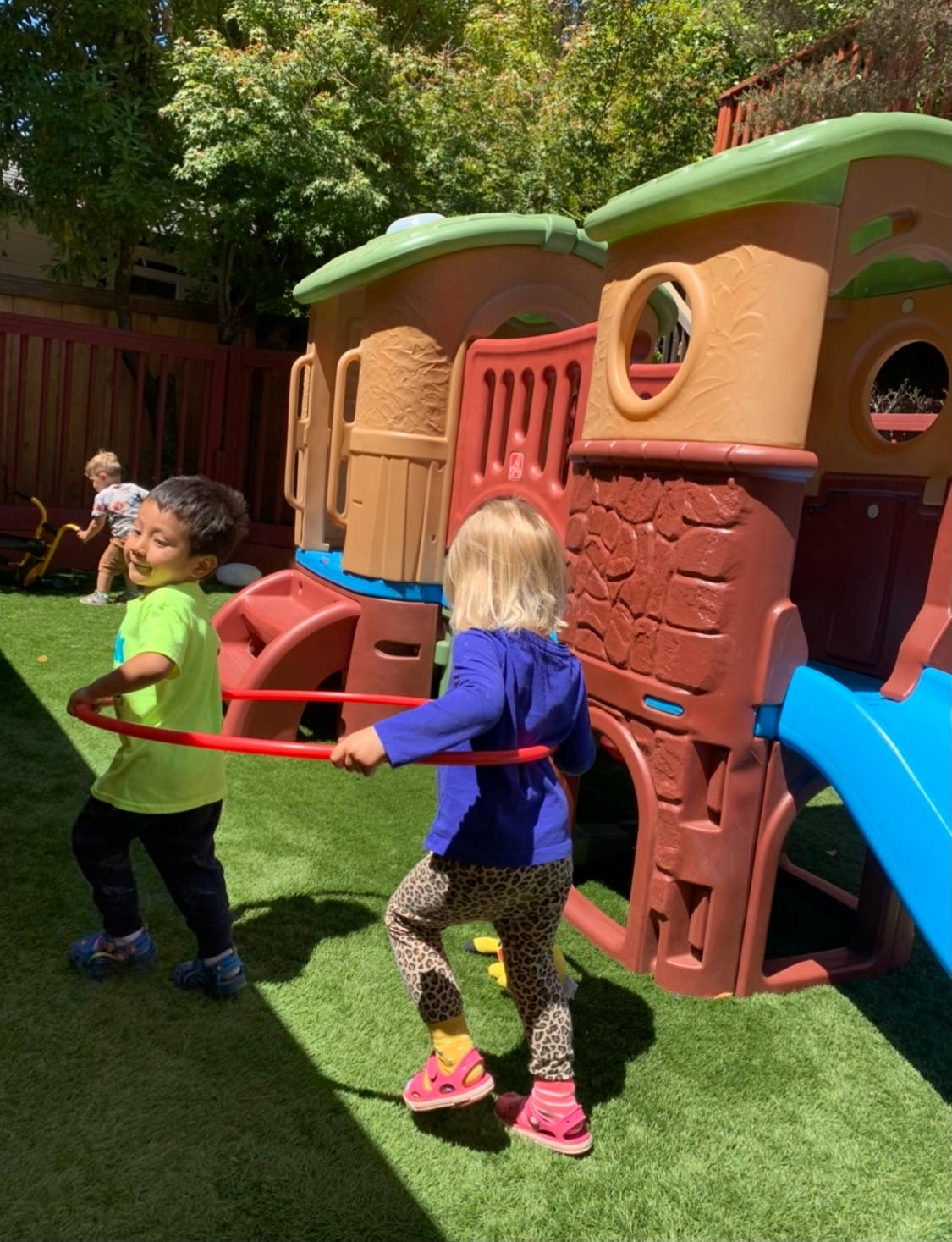 Two children playing with a hula hoop on grass near a play structure