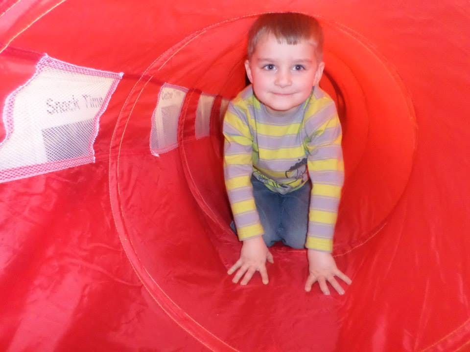 Child crawling through a red play tunnel