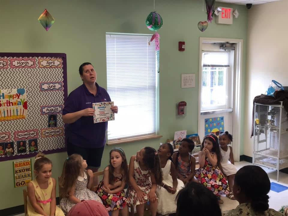 Adult holding paper in front of seated children in a classroom